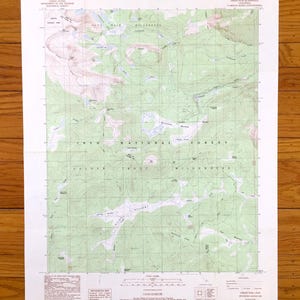 May include: A topographic map of the Inyo National Forest and Golden Trout Wilderness in California. The map features contour lines, water features, and text labels. The map is printed on white paper and is on a wooden surface.
