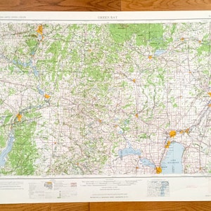 Pode incluir: Um mapa vintage de Green Bay, Wisconsin, impresso em papel branco com um esquema de cores verde claro, azul e laranja. O mapa mostra estradas, rios e lagos da área. O mapa é intitulado "Green Bay" e tem uma escala e uma legenda.