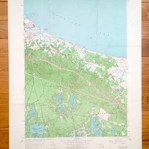 Può includere: Una mappa topografica vintage dell'area di Sandwich, Massachusetts. La mappa mostra la costa, le strade e le masse d'acqua. La mappa è stampata su uno sfondo bianco con linee e testo blu, verdi e marroni.