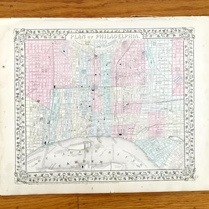 May include: An antique map titled "PLAN OF PHILADELPHIA". The map shows a detailed street grid with areas coloured in pink, blue, and green. The map is framed by a decorative border. The Delaware River is visible at the bottom.