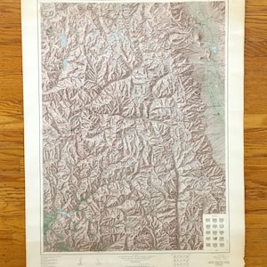 May include: Vintage topographic map of Montana's Glacier National Park and vicinity. The map features detailed contour lines, indicating elevation changes, and includes areas of green and blue, likely representing forests and water bodies. The map is aged with some wear.