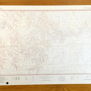 May include: A large, rectangular map with a detailed topographical design. The map features a light beige background with intricate brown and white contour lines, indicating elevation changes. The map is framed with a light pink border and includes text and symbols.