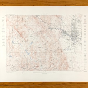 Puede incluir: Un mapa topográfico vintage de Salt Lake City, Utah, con contornos de elevación detallados y características geográficas. El mapa está impreso en papel blanco con líneas azules y rojas.