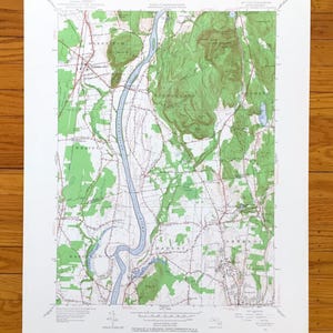 Könnte beinhalten: Eine Vintage-topografische Karte des Connecticut River Valley in Massachusetts. Die Karte zeigt die Städte Deerfield, Whately, Sunderland, Hadley und Amherst. Die Karte ist auf weißem Papier mit grünen, braunen und blauen Linien und Text gedruckt.