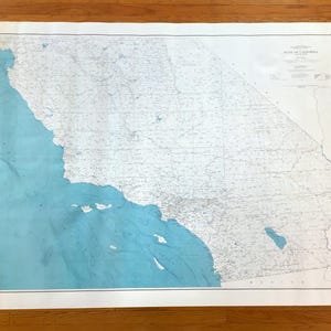 May include: A large, vintage map of California, featuring the state's outline in white against a light blue ocean. The map includes detailed geographical features and place names, with the title "State of California" at the top.