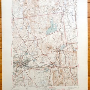 Puede incluir: Un mapa topográfico vintage de Ludlow, Massachusetts, que muestra carreteras, ríos y curvas de nivel. El mapa está impreso en papel color crema con líneas marrones y rojas.