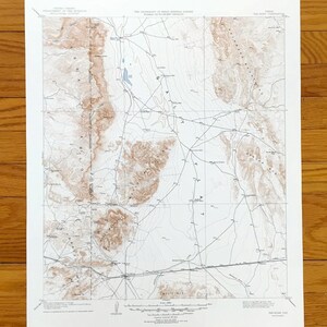 May include: A vintage topographic map in shades of brown and white, showing a landscape with contour lines, roads, and a lake. The map has text at the top and bottom, and is printed on white paper. The map provides a detailed representation of the terrain.