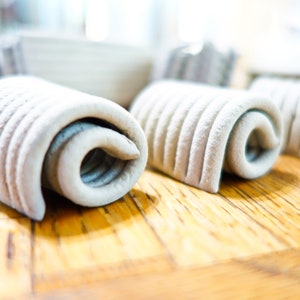 May include: Close-up of four white rolled clay items on a wooden surface. The clay is textured and has a slightly rough appearance.