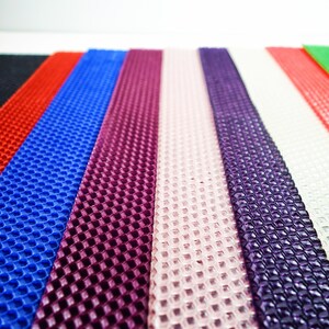 May include: A close-up shot of several colorful sheets of beeswax. The sheets are in various colors, including red, blue, purple, and pink. Each sheet has a honeycomb pattern. The sheets are arranged side by side.