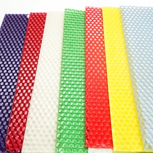 May include: A collection of colorful beeswax sheets in various shades, including purple, red, white, green, yellow, and light blue. Each sheet has a honeycomb pattern, ideal for candle making or craft projects. The sheets are arranged side by side.