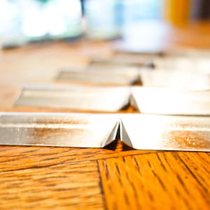 May include: A close-up of a row of silver metal strips folded in half, lying on a wooden surface.