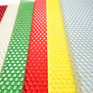 May include: A close-up of several sheets of colorful beeswax. The sheets are red, white, green, yellow, and blue. Each sheet has a honeycomb pattern. The sheets are arranged vertically, with the colors alternating.