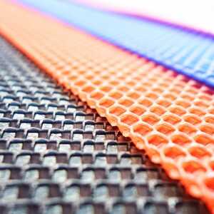 May include: Close-up of three textured mats in shades of black, orange, and blue. The black mat has a woven pattern, while the orange mat features a honeycomb design. The blue mat is smooth. The mats are angled diagonally.