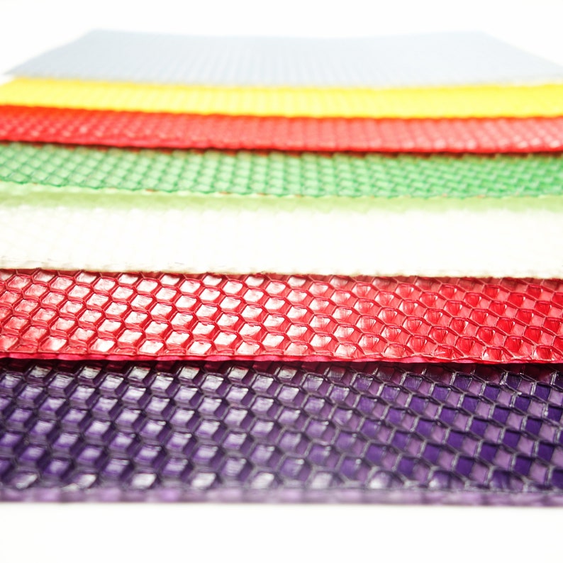 May include: A stack of colorful beeswax sheets in various colors, including gray, yellow, red, green, white, and purple. Each sheet has a honeycomb pattern, and the sheets are stacked on top of each other.