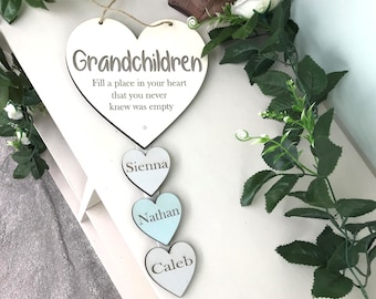 Może przedstawiać: Biała drewniana tabliczka w kształcie serca z tekstem "Grandchildren Fill a place in your heart that you never knew was empty". Trzy mniejsze białe drewniane serca wiszą poniżej z napisami "Sienna", "Nathan" i "Caleb" na nich.