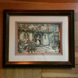 May include: Framed print of a detailed, colorful scene depicting a gathering outside a building. The artwork features figures in period clothing, a woman carrying a tray, and animals. The frame is dark brown.