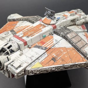 May include: A detailed model spacecraft with a distressed finish. The ship is predominantly white and orange, with red and yellow highlights. The model displays intricate detailing, including a cockpit and various mechanical elements. The model is approximately 20 cm long.