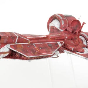 May include: A detailed model of a red and white spaceship with a weathered appearance. The spacecraft features a central body with wing-like extensions and circular engine components. The model is set against a white background.