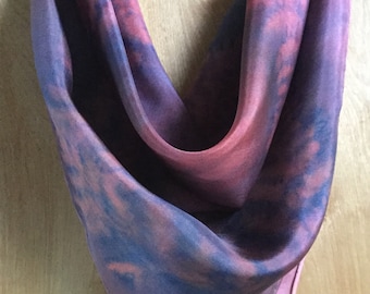 Könnte beinhalten: Ein rosa-blauer Seidenschal mit einem Batik-Muster. Der Schal ist gefaltet und auf einer Holzoberfläche ausgestellt.