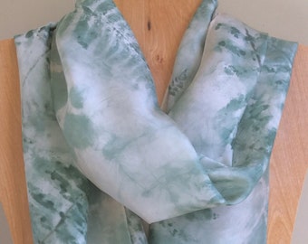 Könnte beinhalten: Ein hellgrüner und weißer Seidenschal mit einem Batik-Muster. Der Schal ist gefaltet und auf einer Holzpuppe ausgestellt.