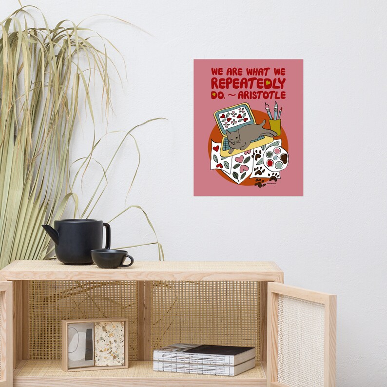 May include: A pink background with a cat sitting on a laptop computer. The cat is surrounded by paintbrushes, paint, and hearts. The text "We are what we repeatedly do. ~Aristotle" is written in red and white.