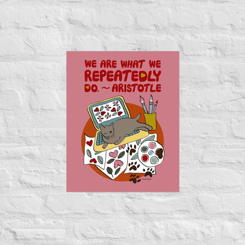 May include: A pink background with a quote from Aristotle: "We are what we repeatedly do." The quote is in red text with a heart symbol. A gray cat is lying on a laptop computer with a paint palette, paintbrushes, and papers with hearts and paw prints on them.