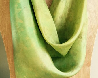 Könnte beinhalten: Ein grüner Seidenschal mit einem Batik-Muster. Der Schal ist gefaltet und auf einer Holzpuppe ausgestellt.