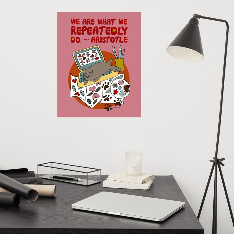 May include: A pink poster with a quote from Aristotle: "We are what we repeatedly do." The quote is illustrated with a cat sitting on a laptop surrounded by paintbrushes, paint, and paw prints.