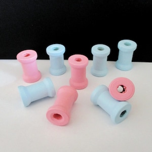 May include: A collection of wooden spools painted in light blue and pink. The spools are arranged on a white surface.
