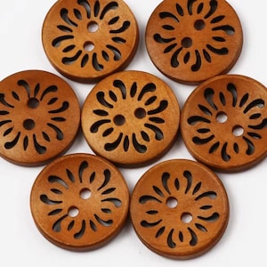 May include: Seven round wooden buttons with a floral design. Each button is a warm brown colour and features cut-out shapes around the centre holes. The buttons are arranged on a white surface.