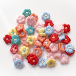 May include: A collection of colorful, embroidered flower appliques in various shades of red, pink, yellow, blue, and orange. The flowers are small, with detailed stitching and a central contrasting color.