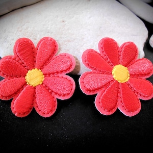 May include: Two red embroidered daisy flower patches with yellow centers. The petals are outlined with a darker red thread. These patches are perfect for adding a floral touch to clothing or accessories.