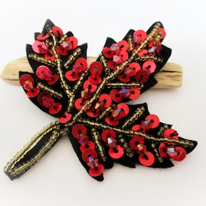 May include: A red and gold sequined leaf brooch with a black felt backing. The leaf is made of sequins and beads, and the stem is made of gold beads.