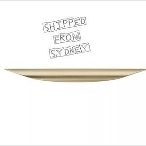 May include: A brushed gold, curved cabinet handle. The handle is approximately 30 cm long.