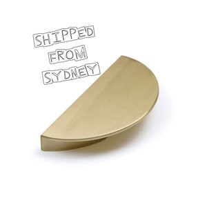May include: A half-round, brushed brass cabinet pull. The pull is a simple, modern design.