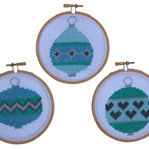 Può includere: Tre ornamenti natalizi ricamati in cerchi di legno. Ogni ornamento presenta un design diverso: un ornamento blu e verde con stelle, un ornamento blu e verde con un motivo a zig-zag e un ornamento blu e verde con un motivo a cuore.