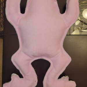 May include: A pink frog-shaped plush toy with a simple design. The toy is made of soft fabric and has a smooth, even texture.
