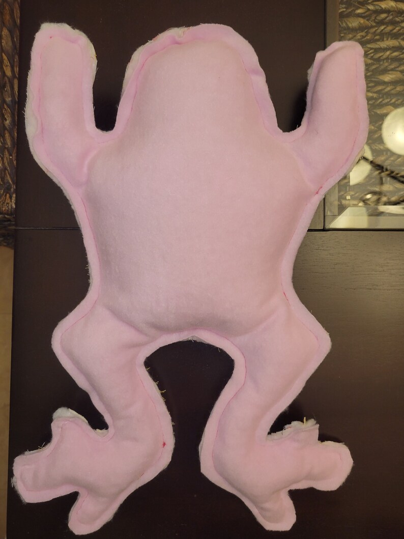 May include: A pink frog-shaped plush toy with a simple design. The toy is made of soft fabric and has a smooth, even texture.