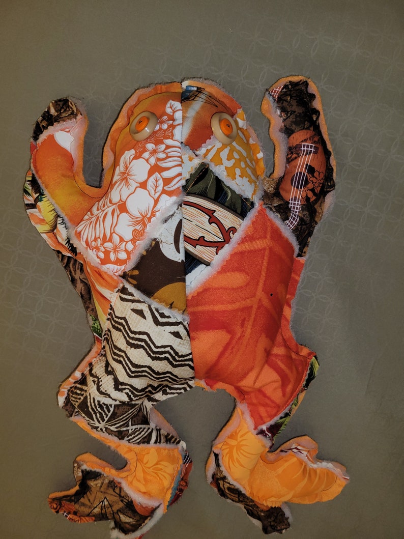 May include: A patchwork frog toy made from colorful fabric scraps. The frog has orange, brown, white, and black fabric with a floral pattern. The frog has large orange eyes.