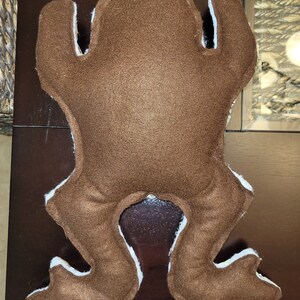 May include: Brown felt frog plush toy with white felt accents. The frog is lying on its back with its legs outstretched.