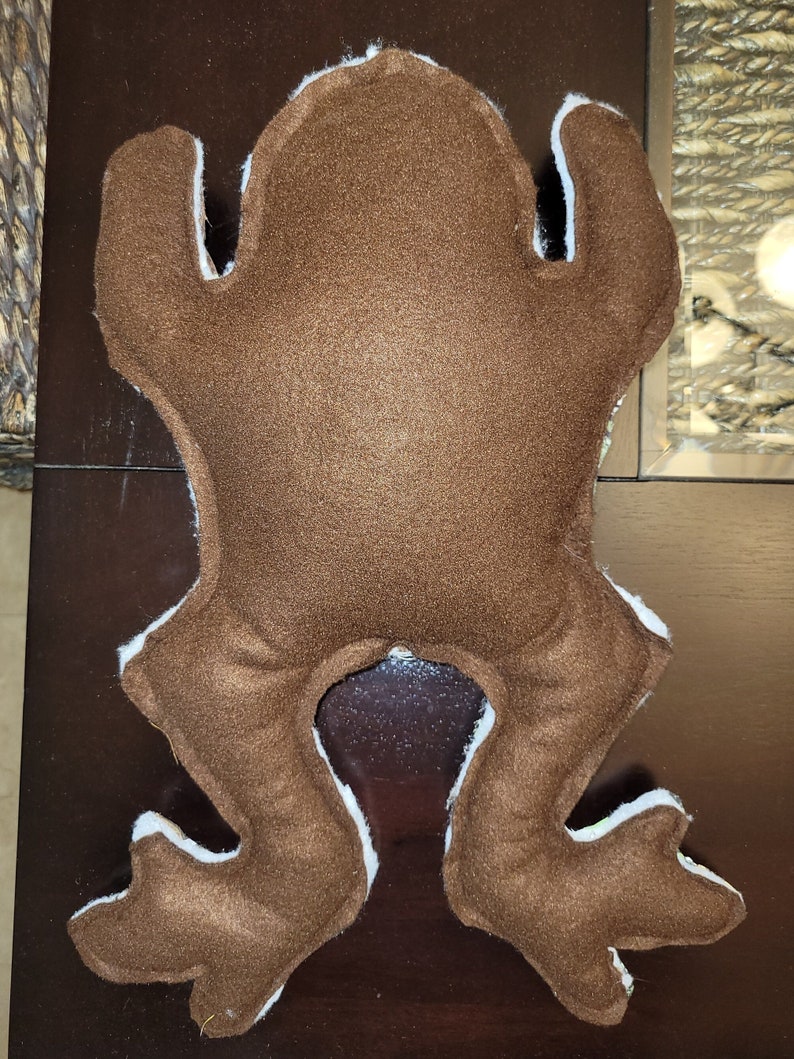 May include: Brown felt frog plush toy with white felt accents. The frog is lying on its back with its legs outstretched.