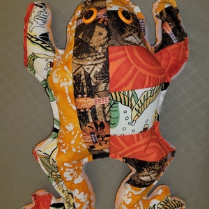 May include: A patchwork frog toy with orange, brown, green, and white fabric. The frog has large, yellow button eyes.