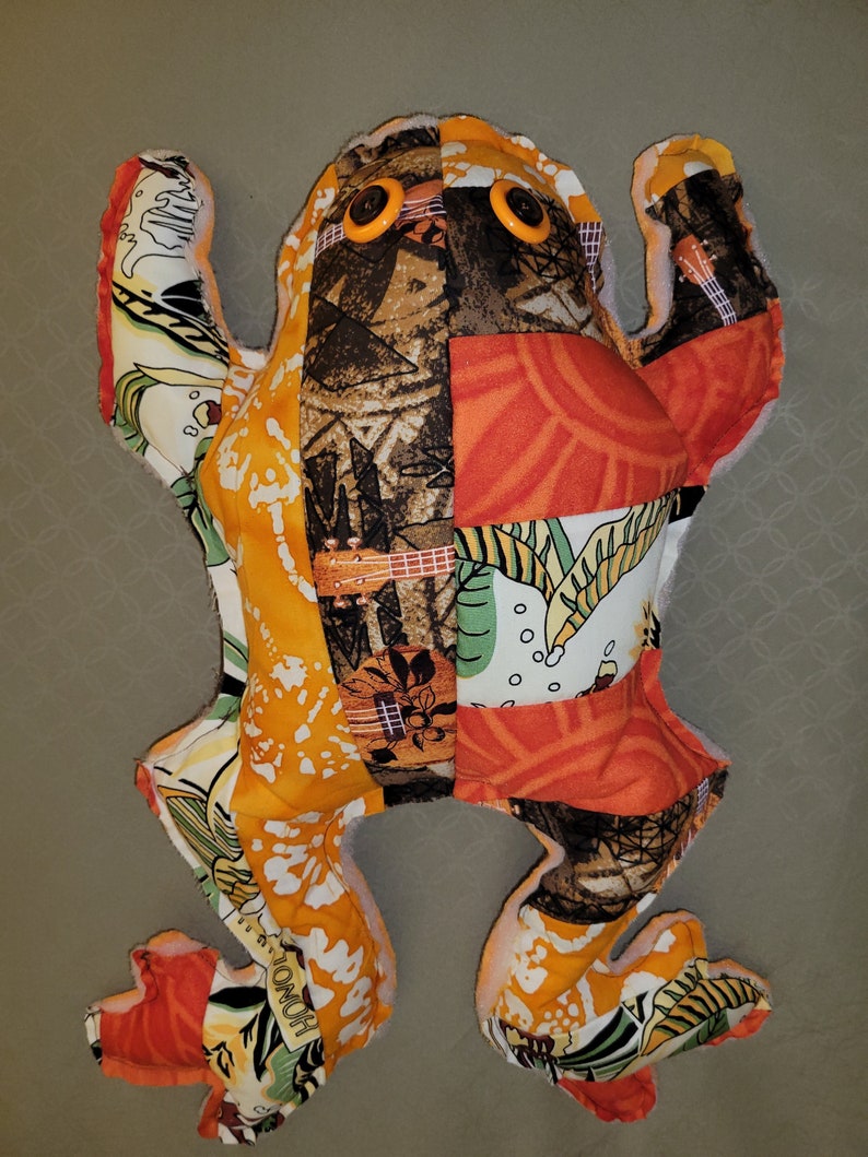 May include: A patchwork frog toy with orange, brown, green, and white fabric. The frog has large, yellow button eyes.
