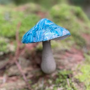 Puede incluir: Un hongo azul y blanco marmoleado con un tallo gris. El hongo está sentado en un lecho de musgo.