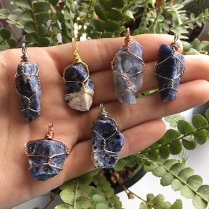 May include: Six wire-wrapped blue and white gemstone pendants. The pendants are wrapped in gold and copper wire and are displayed on a hand.