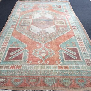 Puede incluir: Una alfombra rectangular de aspecto desgastado, con un dise&ntilde;o geom&eacute;trico central en tonos coral, turquesa y burdeos. La alfombra presenta un borde detallado y flecos, adecuada para la decoraci&oacute;n del hogar, en cm.