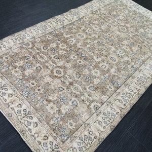 Puede incluir: Alfombra rectangular beige con estampado floral y borde decorativo. La alfombra presenta un campo central en tonos beige y marrón con detalles azules. El borde es de color beige claro con diseños florales y de hojas.