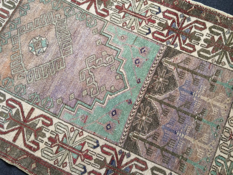 May include: A rectangular, vintage rug with a patchwork design. The rug features a palette of muted colours, including shades of brown, purple, and teal. Geometric and floral patterns are visible throughout the rug's surface, creating a textured appearance.