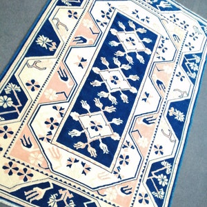 May include: A rectangular rug with a geometric pattern. The rug features a navy blue central design with cream and light pink accents. The border is navy blue, and the rug has a traditional, ornate style.
