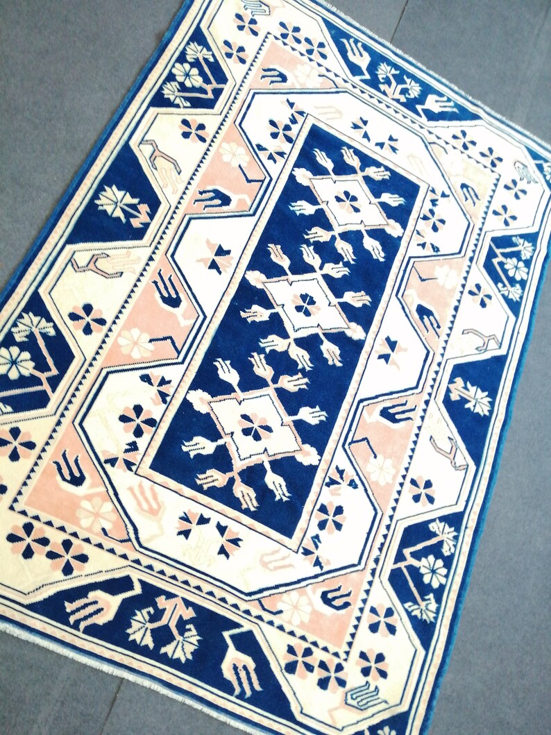 May include: A rectangular rug with a geometric pattern. The rug features a navy blue central design with cream and light pink accents. The border is navy blue, and the rug has a traditional, ornate style.